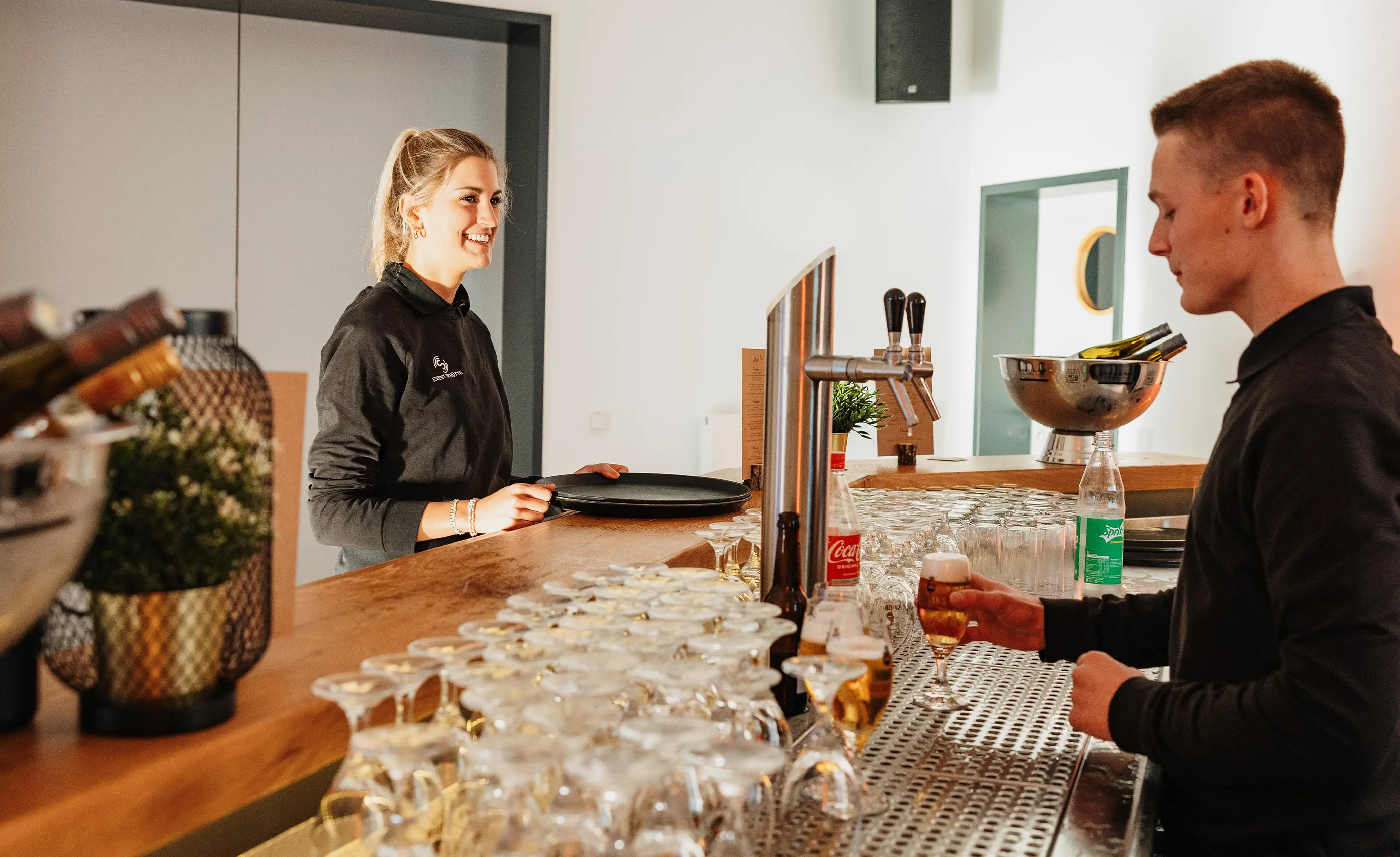 Zwei Mitarbeiter stehen an einer Theke und einer zapft Bier